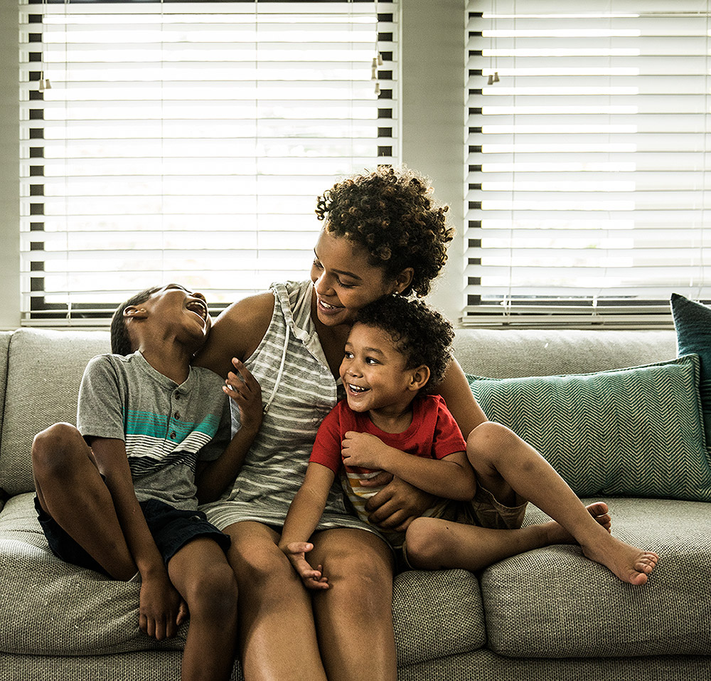 Photo of smiling family, mother and young sons, playing on the couch